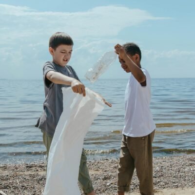 Two boys clean a beach, picking up litter to promote environmental sustainability.