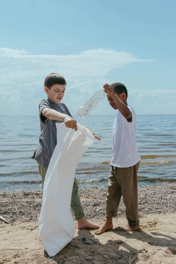 Two boys clean a beach, picking up litter to promote environmental sustainability.